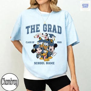 Puede incluir: Camiseta azul claro con el texto "THE GRAD" en azul marino, junto con "CLASS OF 2026" y un dibujo animado de personajes de Disney con gorros de graduaci&oacute;n. La camiseta tambi&eacute;n incluye espacio para el nombre de la escuela.