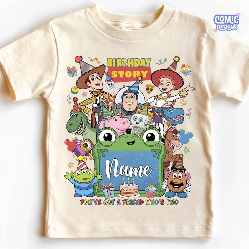May include: A cream-colored t-shirt featuring a colorful graphic of Toy Story characters wearing party hats. The text reads Birthday Story, Name, and You've Got A Friend Who's Two. The design includes Woody, Buzz Lightyear, Jessie, and other characters surrounding a green frog-shaped frame.