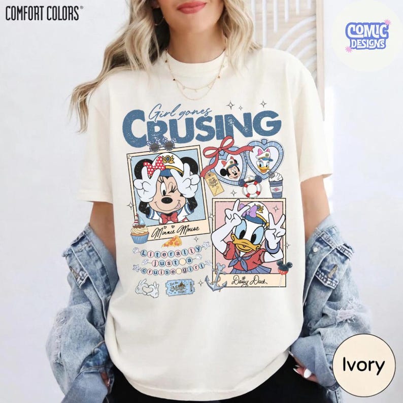 以下が含まれることがあります： アイボリー色のTシャツ。ミニーマウスとドナルドダックがセーラー服を着たグラフィックで、「Girl goes Cruising」の文字が入っています。デザインには額縁に入った画像と航海要素が含まれています。このシャツはComfort Colors製です。