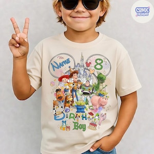 以下が含まれることがあります： ベージュ色のTシャツ。トイ・ストーリーのキャラクター、お城、数字の8がカラフルに描かれています。「Name」と「Birthday Boy」の文字も含まれています。Tシャツは人が着ています。