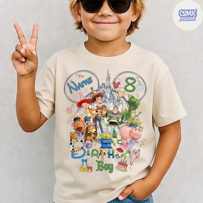 以下が含まれることがあります： ベージュ色のTシャツ。トイ・ストーリーのキャラクター、お城、数字の8がカラフルに描かれています。「Name」と「Birthday Boy」の文字も含まれています。Tシャツは人が着ています。