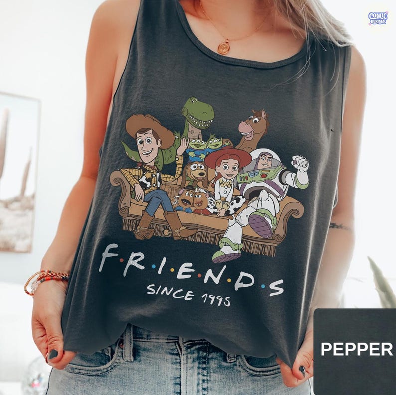 May include: A dark gray sleeveless tank top featuring a graphic print of various animated characters sitting on a couch. Below the illustration, the white text reads "F R I E N D S" with colorful dots between the letters, followed by "SINCE 1995".