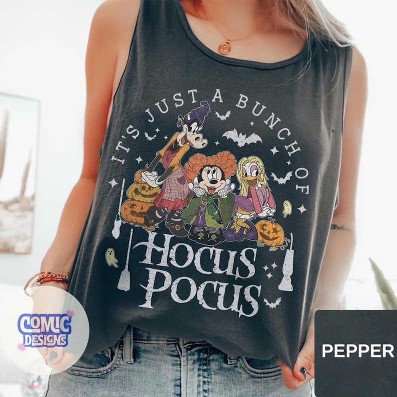 May include: A charcoal gray sleeveless tank top featuring a graphic print of three cartoon characters dressed as witches, surrounded by pumpkins, bats, and ghosts. The text reads, IT'S JUST A BUNCH OF HOCUS POCUS, in a distressed white font.