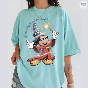 May include: A turquoise t-shirt with a cartoon image of Mickey Mouse in a wizard outfit, wielding a magic wand. The text "Some imagination huh?" is above the character. The shirt has a loose fit and short sleeves.