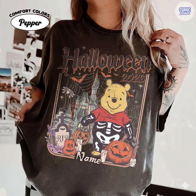 May include: Black Comfort Colors t-shirt with a Halloween graphic. It features a cartoon bear in a skeleton costume, pumpkins, and a haunted castle. The text "Halloween 2023" is above the bear, and "Name" is below.