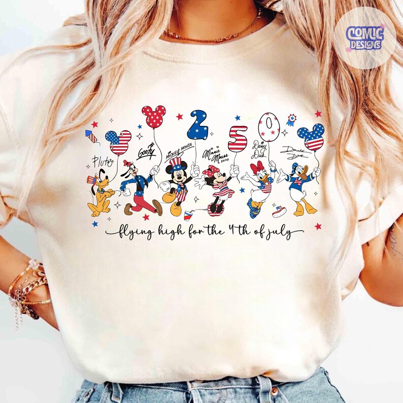 May include: Cream-colored t-shirt featuring Disney characters celebrating the 4th of July. Pluto, Goofy, Mickey, Minnie, Daisy, and Donald Duck are depicted holding balloons. The text "flying high for the 4th of July" is written below the characters.