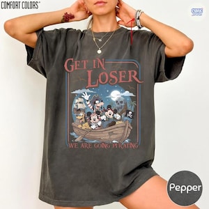 May include: Pepper-colored t-shirt with a pirate-themed graphic. The design features Mickey Mouse, Goofy, and other characters in a boat with the text "Get In Loser, We Are Going Pirating". The shirt is from Comfort Colors.