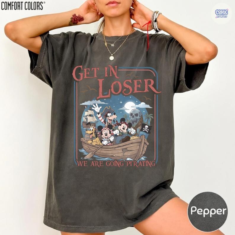 May include: Pepper-colored t-shirt with a pirate-themed graphic. The design features Mickey Mouse, Goofy, and other characters in a boat with the text "Get In Loser, We Are Going Pirating". The shirt is from Comfort Colors.