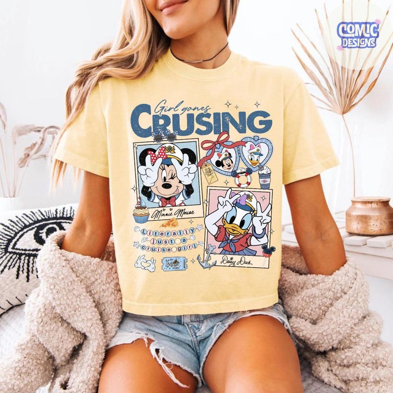 以下が含まれることがあります： ミニーマウスとドナルドダックのグラフィックと「Girl goes Cruising」の文字が入った、明るい黄色のTシャツ。 ヴィンテージ感のあるデザインで、漫画の画像とテキスト要素が含まれています。