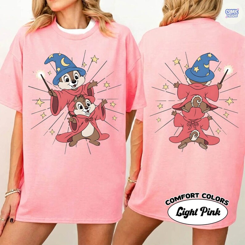Puede incluir: Camiseta rosa claro con una ilustraci&oacute;n de dibujos animados de dos ardillas vestidas de magos, con un sombrero azul y una varita. La parte trasera de la camiseta tambi&eacute;n tiene el mismo dise&ntilde;o. El texto "COMFORT COLORS Light Pink" est&aacute; impreso en la parte inferior.