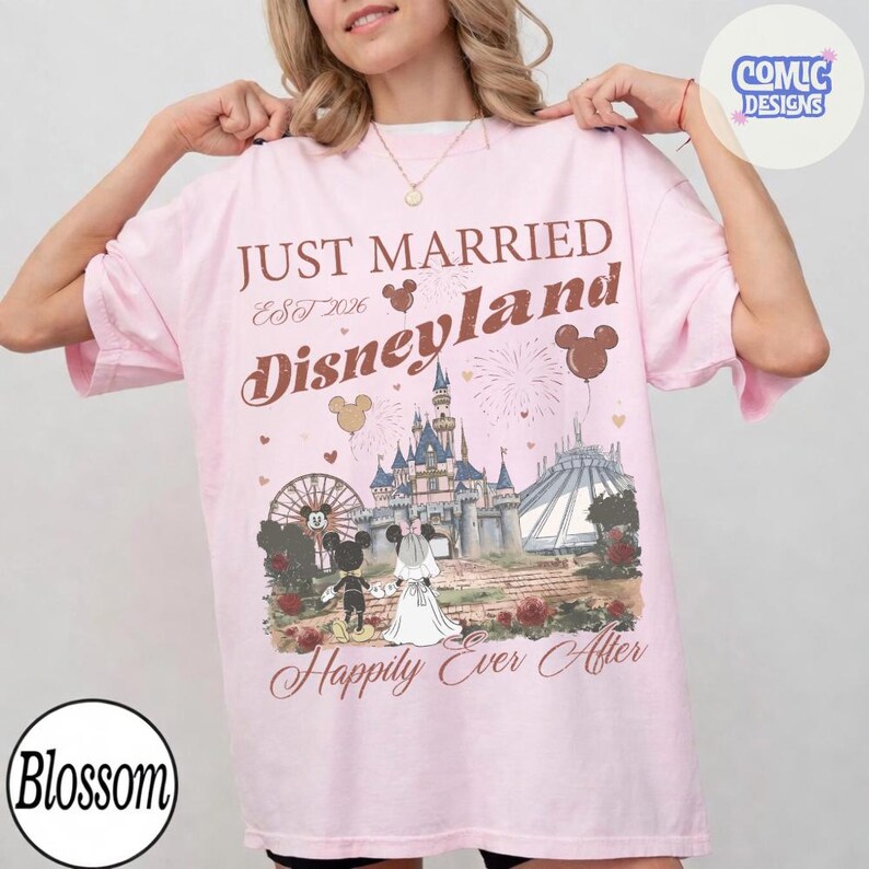 May include: A light pink t-shirt with the words "JUST MARRIED Disneyland" in brown script. The shirt features a graphic of the Disneyland castle, Mickey and Minnie Mouse, and the phrase "Happily Ever After."
