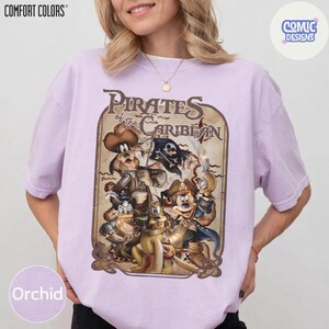 May include: Orchid-colored t-shirt featuring a vintage-style graphic of Disney characters as pirates, with the text "Pirates of the Caribbean." The shirt has a crew neck and short sleeves. The brand name "COMFORT COLORS" is printed at the top left.