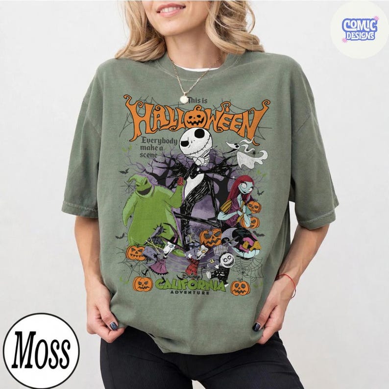 May include: Olive green t-shirt featuring a Halloween-themed graphic. The design includes Jack Skellington, Sally, and other characters, with the text "This is Halloween" and "California Adventure".