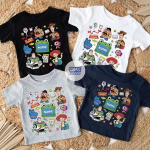 May include: Four short-sleeve t-shirts in black, white, gray, and navy blue, each featuring a colorful graphic print of cartoon characters including a cowboy, space ranger, potato figure, and a green frog frame with the text Name.