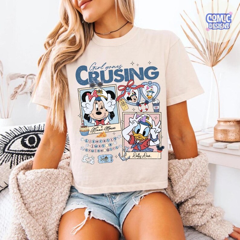 以下が含まれることがあります： ミニーマウスとドナルドダックのグラフィックが特徴のクリーム色のTシャツ。「Girl goes Cruising」の文字が青色でデザインされており、他のグラフィックやテキストも含まれています。半袖のシャツです。