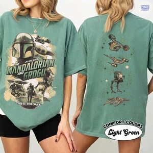 Op de afbeelding: Lichtgroen T-shirt met een "The Mandalorian and Grogu" ontwerp. De voorkant toont de Mandalorian helm, Grogu en de tekst "This is the Way". De achterkant toont Star Wars voertuigen. "Comfort Colors" en "Light Green" zijn ook zichtbaar.