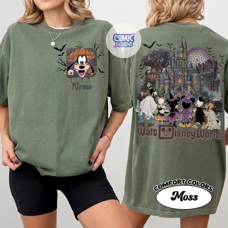 May include: An olive green t-shirt featuring a front graphic of Goofy wearing a pumpkin hat and a back graphic of Disney characters in Halloween costumes standing before a castle with the text Walt Disney World and Comic Designs.