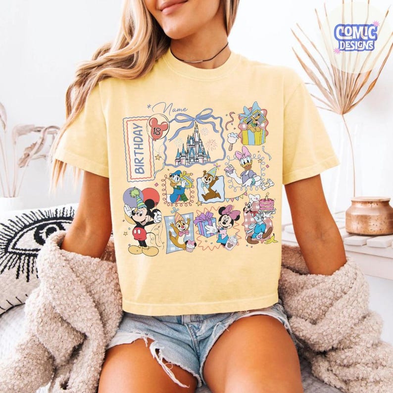 May include: Yellow t-shirt featuring a colorful graphic of Disney characters celebrating a birthday. The design includes Mickey Mouse, Minnie Mouse, Donald Duck, and other characters, along with a castle and the word "Birthday".