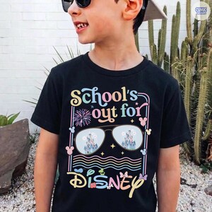 Może przedstawiać: Czarny t-shirt z napisem "School's out for Disney" w kolorowych literach. Projekt zawiera okulary przeciwsłoneczne odbijające zamek, fajerwerki i ikony Myszki Miki. Zabawna koszulka dla dzieci.