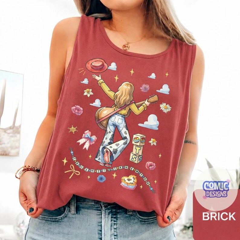 May include: A brick red sleeveless tank top featuring a graphic illustration of a person with long hair playing a guitar, wearing cow print bell-bottom pants and a hat. The design includes flowers, clouds, stars, a bow, and blocks with the text BTS.