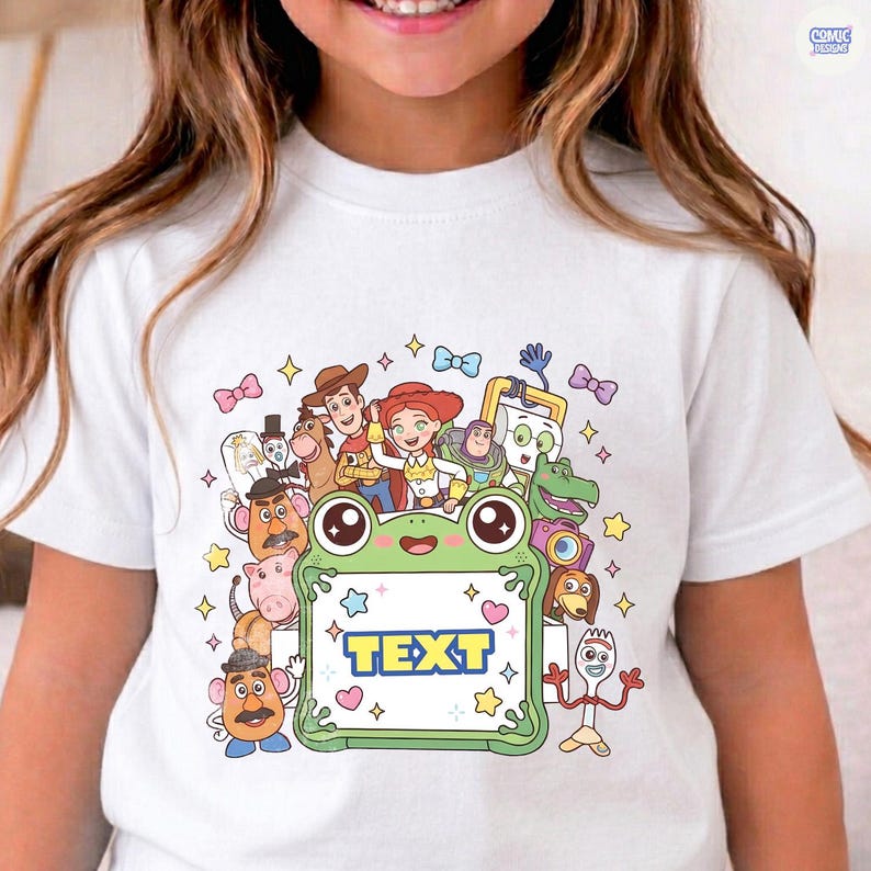 May include: A white short-sleeved t-shirt featuring a colorful graphic print of various animated characters surrounding a central light green frog-shaped frame. The frame contains the word TEXT in bold blue letters, accented by small stars and hearts.