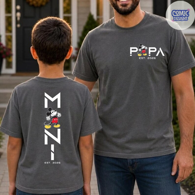 May include: Two gray t-shirts with Mickey Mouse graphics. One shirt says "PAPA" with Mickey and "EST. 2026". The other shirt has "M" and "Z" with Mickey and "EST. 2026".