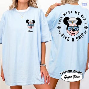 May include: Light blue t-shirt featuring a cartoon mouse wearing a sailor hat and sunglasses. The front of the shirt has the word "Name" below the mouse. The back of the shirt says "This week we don't give a ship."