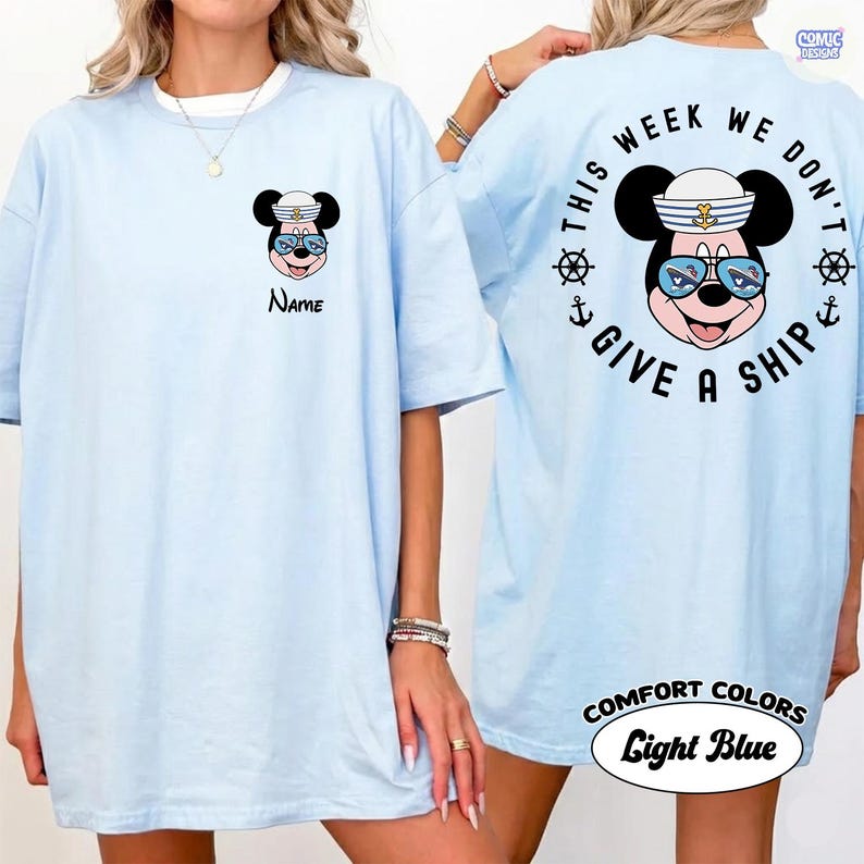 May include: Light blue t-shirt featuring a cartoon mouse wearing a sailor hat and sunglasses. The front of the shirt has the word "Name" below the mouse. The back of the shirt says "This week we don't give a ship."