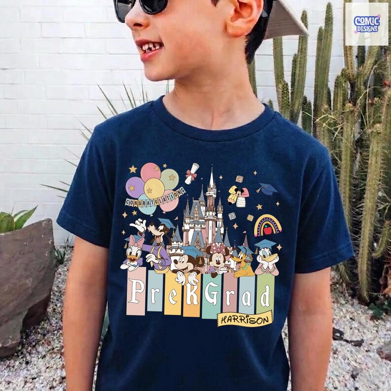 May include: Navy blue t-shirt featuring a colorful graphic of Disney characters, a castle, balloons, and a rainbow. The shirt says "Prek Grad" and "Harrison". The design includes Mickey and Minnie Mouse, Donald and Daisy Duck, and other characters.