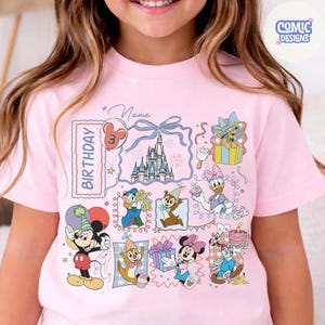 May include: Pink short-sleeved t-shirt featuring a colorful Disney-themed birthday design. The design includes various cartoon characters, a castle, and the word "Birthday". The shirt also has the text "Comic Designs".