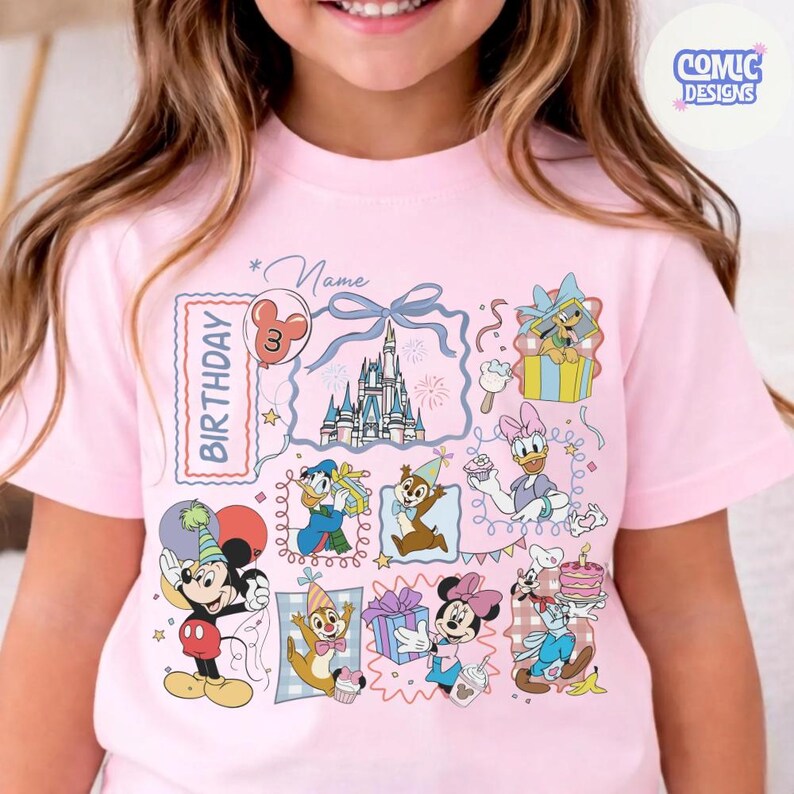 May include: Pink short-sleeved t-shirt featuring a colorful Disney-themed birthday design. The design includes various cartoon characters, a castle, and the word "Birthday". The shirt also has the text "Comic Designs".