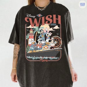Puede incluir: Camiseta negra con un gr&aacute;fico colorido de personajes de Disney en un crucero. El dise&ntilde;o incluye las palabras "Disney Wish 2026" y un faro. La camiseta tiene un aspecto vintage y desgastado.