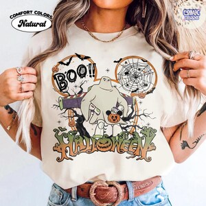 Peut inclure: Un t-shirt de couleur naturelle avec un motif repr&eacute;sentant un personnage d&eacute;guis&eacute; en fant&ocirc;me portant une combinaison de ranger de l'espace. Le design inclut le texte "BOO!!" et "HALLOWEEN", une toile d'araign&eacute;e, des chauves-souris et une citrouille.