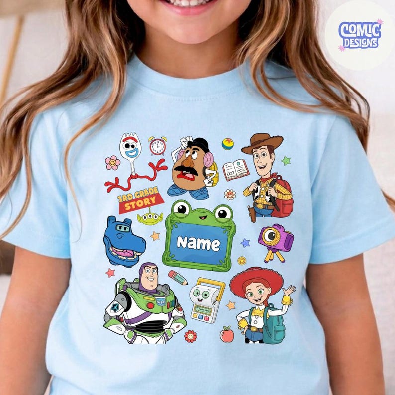 May include: A light blue t-shirt featuring a colorful graphic print of Toy Story characters including Woody, Buzz Lightyear, Jessie, Mr. Potato Head, and Forky. The design includes a green frog-shaped frame with the text Name and 3rd Grade Story.