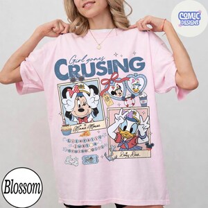 以下が含まれることがあります： 「Girl goes Cruising」の青い文字が入った薄いピンク色のTシャツ。ミニーマウスとデイジーダックがセーラー服を着たイラストと、航海をテーマにしたグラフィックが特徴です。