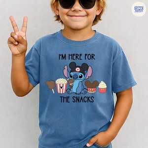 May include: Blue t-shirt featuring Stitch from Lilo & Stitch with the text "I'M HERE FOR THE SNACKS." Stitch is wearing a Mickey Mouse hat and holding a snack. The shirt also has images of popcorn, ice cream, and cupcakes.