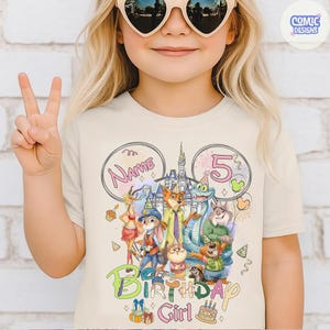 以下が含まれることがあります： クリーム色のTシャツ。カラフルなグラフィックデザインが特徴です。「Birthday Girl」の文字と数字の「5」、様々な漫画のキャラクター、お城が描かれています。「Name」の文字も含まれています。