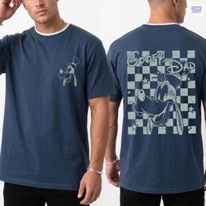 May include: Navy blue t-shirt featuring a Goofy graphic on the front and back. The back design includes the text "Goofy Dad" over a checkered pattern. The shirt has a white crew neck and short sleeves.