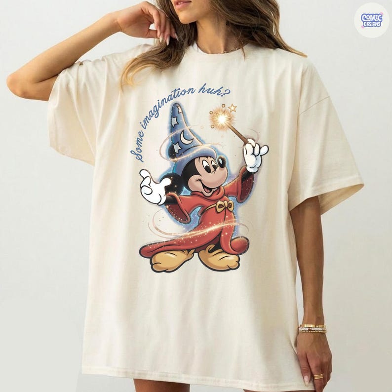 May include: A cream-coloured t-shirt with a cartoon Mickey Mouse as a wizard, holding a wand with a sparkling star. The text "some imagination huh?" is written in a whimsical font. The shirt has a relaxed fit.