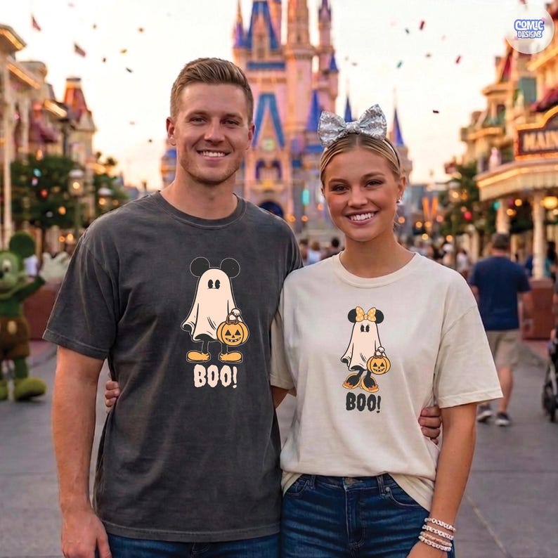 May include: Two people wearing matching Halloween-themed t-shirts. The shirts feature a cartoon ghost with Mickey Mouse ears holding a jack-o'-lantern and the word "BOO!". One shirt is dark gray, the other is cream-colored.