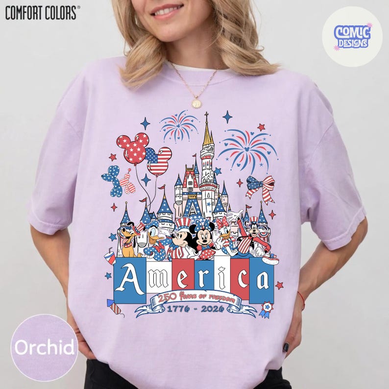 May include: A light purple short-sleeve t-shirt featuring a graphic of a castle, fireworks, and cartoon characters wearing patriotic red, white, and blue clothing. The text reads America, 250 Years of Freedom, and 1776-2026 in a banner below.