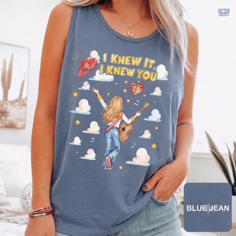 May include: A blue denim-colored tank top featuring a graphic of a person with long blonde hair playing an acoustic guitar. The text reads I KNEW IT, I KNEW YOU, accompanied by a red cowboy hat, a heart with TS, yellow stars, and white clouds.