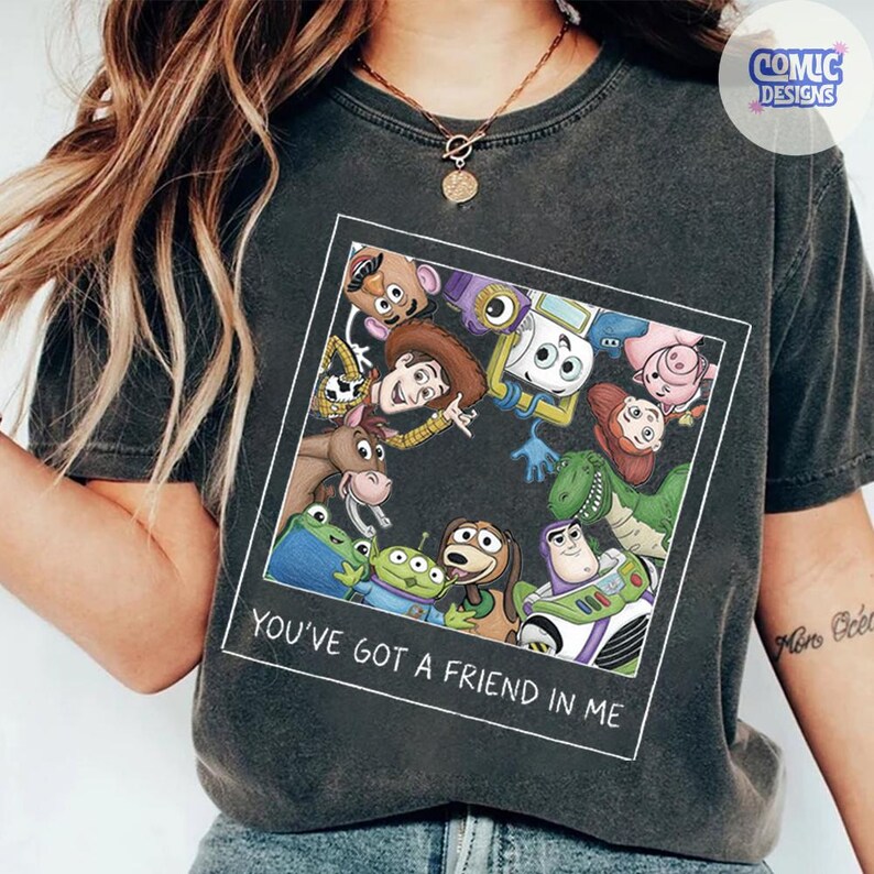 May include: A charcoal gray t-shirt featuring a square graphic print of various animated characters from the Toy Story franchise. Below the characters, the text reads, "YOU'VE GOT A FRIEND IN ME." The shirt has a crew neckline and short sleeves.
