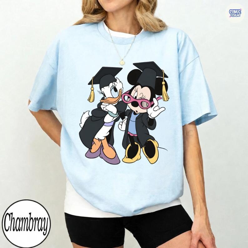 Puede incluir: Camiseta azul claro con un dise&ntilde;o de Donald Duck y Minnie Mouse con atuendos de graduaci&oacute;n. Donald Duck lleva una toga y un gorro negros con una borla dorada. Minnie Mouse lleva gafas rosas y un atuendo de graduaci&oacute;n a juego. La camiseta tiene la palabra "Chambray".