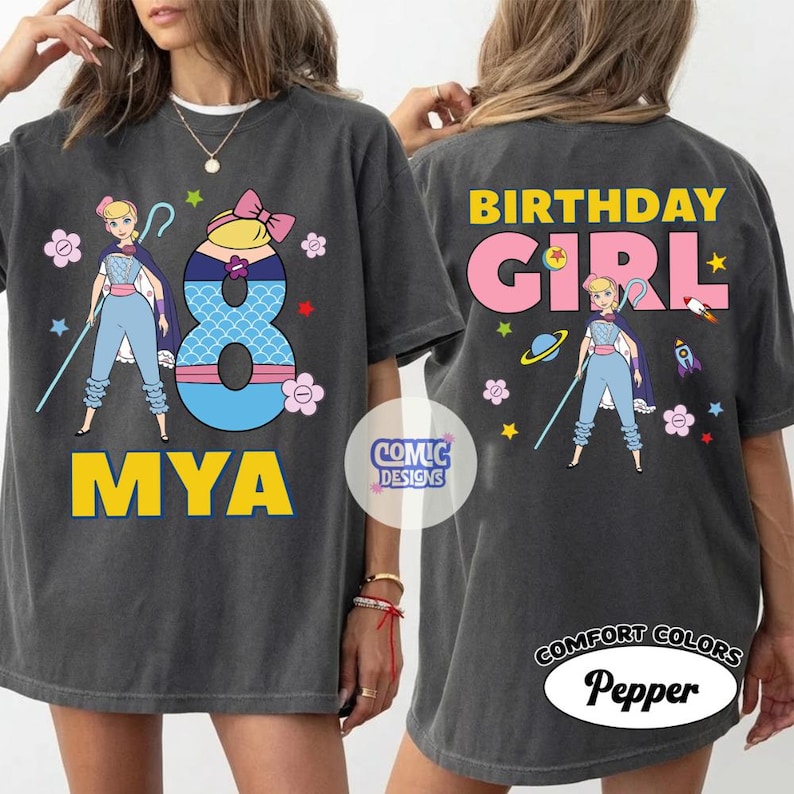 Puede incluir: Camiseta gris oscuro con un dise&ntilde;o de personaje de dibujos animados, el n&uacute;mero 8 y el nombre "MYA" en amarillo. La parte trasera de la camiseta dice "BIRTHDAY GIRL". La camiseta est&aacute; etiquetada como "COMFORT COLORS Pepper".