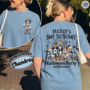 Puede incluir: Camiseta azul claro Comfort Colors Chambray con dise&ntilde;o de Halloween. La parte delantera tiene un gr&aacute;fico de esqueleto de Minnie Mouse con una telara&ntilde;a. La parte trasera muestra "Mickey's Not So Scary Halloween Party" con personajes de Disney esquel&eacute;ticos.