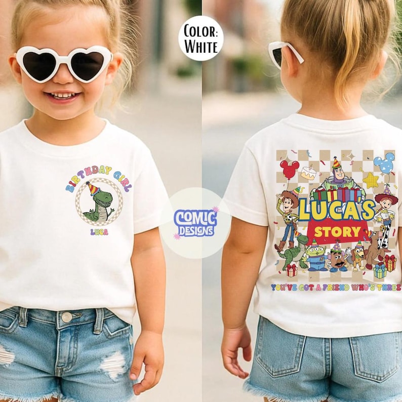 May include: White t-shirt with a dinosaur graphic and the text "BIRTHDAY GIRL" and the name "LUKA". The back of the shirt has a "LUCAS'S STORY" design with cartoon characters. The shirt is worn by a child.