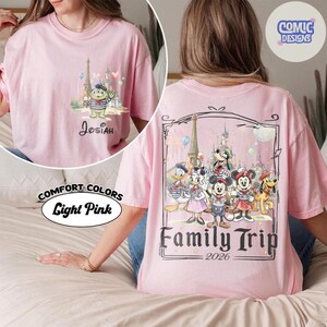May include: A light pink t-shirt featuring a small graphic on the front left chest of a green alien character in front of a castle with the name Josiah. The back displays a large graphic of Disney characters in front of a castle with the text Family Trip 2026.