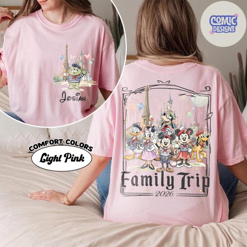 May include: A light pink t-shirt featuring a small graphic on the front left chest of a green alien character in front of a castle with the name Josiah. The back displays a large graphic of Disney characters in front of a castle with the text Family Trip 2026.