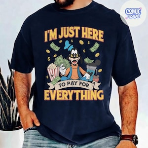 May include: Navy blue t-shirt with a graphic of Goofy holding money and popcorn, with the text "I'M JUST HERE TO PAY FOR EVERYTHING". The design includes dollar signs and a Mickey Mouse-themed drink.